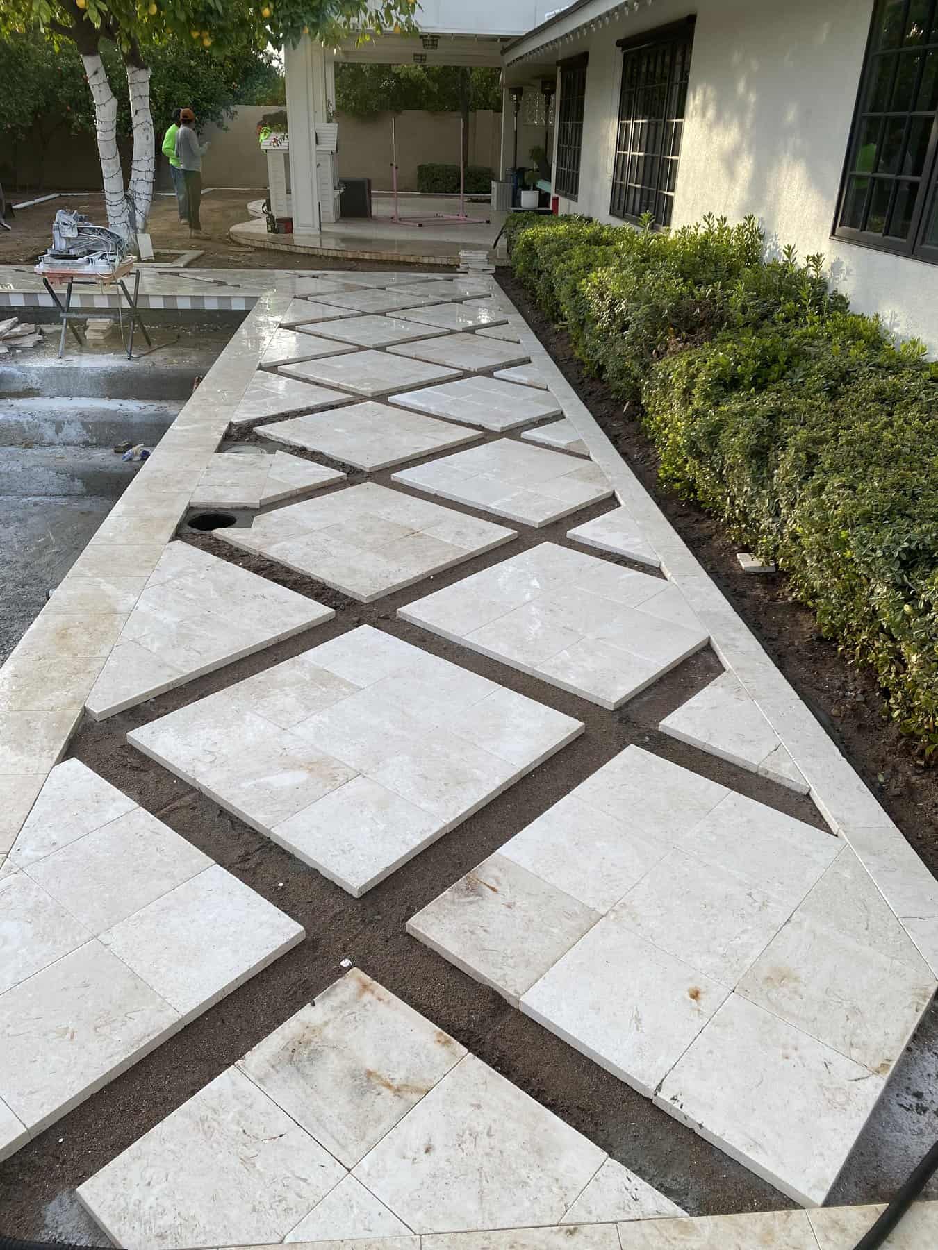 Enjoy a backyard retreat featuring a concrete patio, white stucco pillars, artificial grass, tiled flooring, and white brick walls. Landscaping rocks line the edges—expertly crafted by your trusted Pavers Installer Texas.