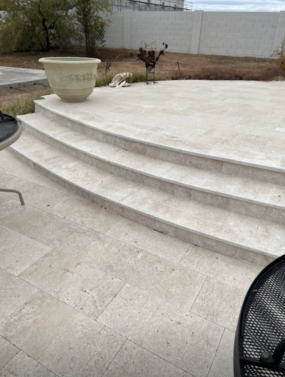 Outdoor stone steps under construction, featuring light gray rectangular pavers in a staggered pattern leading to a house. Dirt and a wheelbarrow are visible to the right—work expertly handled by a Pavers Installer Texas specialist.