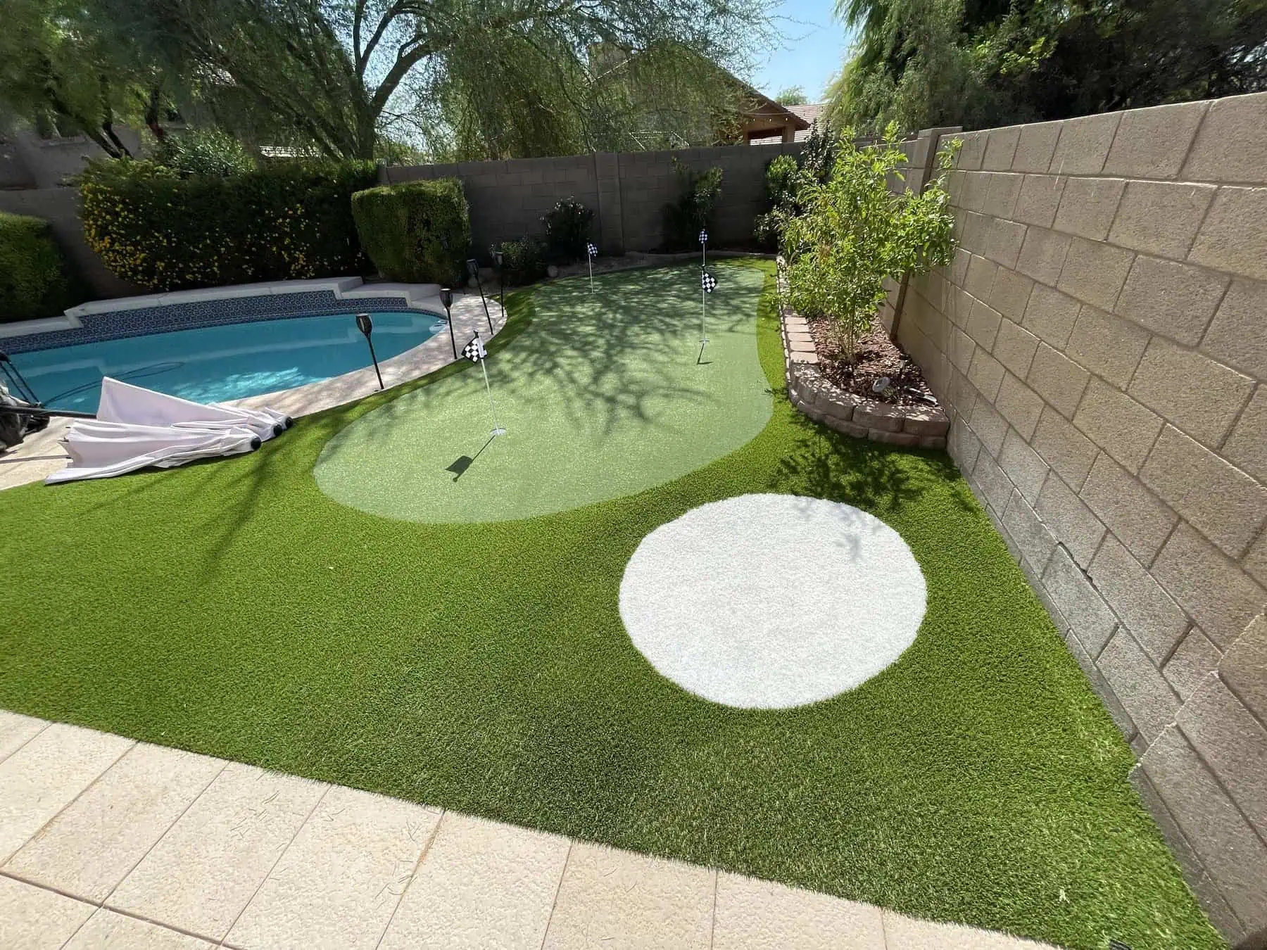 A white dog with one floppy ear and one upright ear is lounging on vibrant pet turf, facing forward and smiling. Its tail is relaxed, and the artificial grass beneath looks freshly cut and lush.